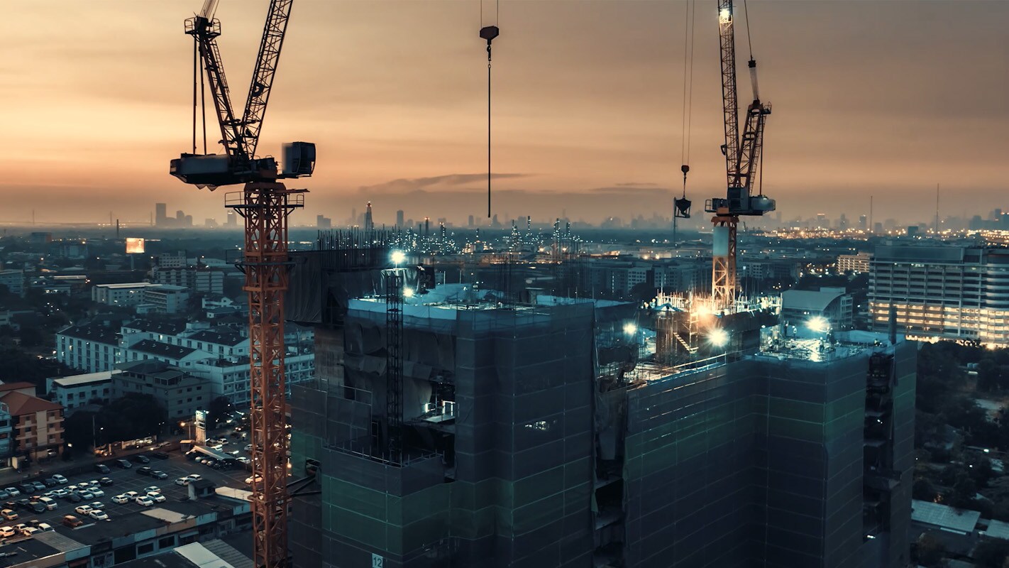 A view overlooking the construction of new buildings with a cityscape in the middle ground and an orange-coloured horizon in the background.