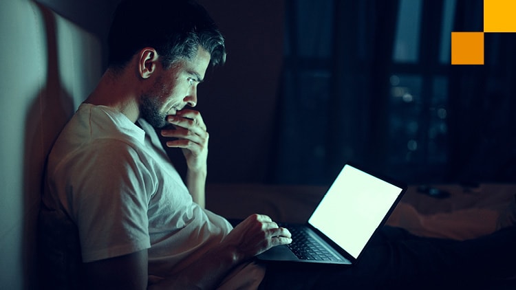 A photo of a young man using his laptop in a dark room.