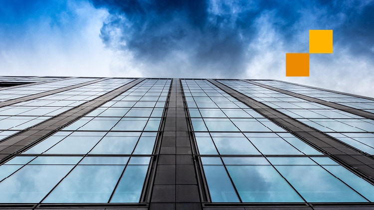 A photo of the side of a modern building, looking upwards towards a bright sky with some clouds.