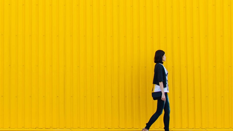 A woman walking in front of a yellow container.
