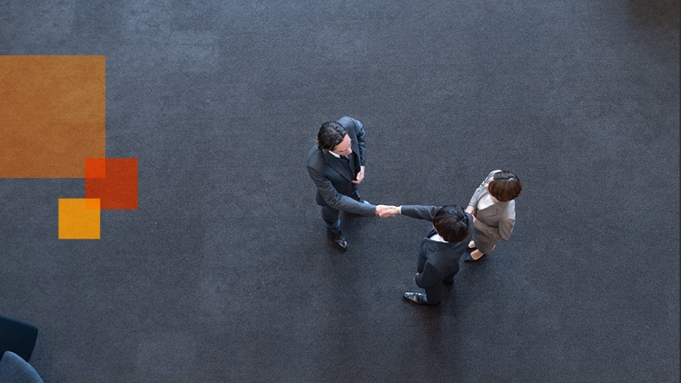 A picture taken from above looking down on three people meeting and shaking hands.