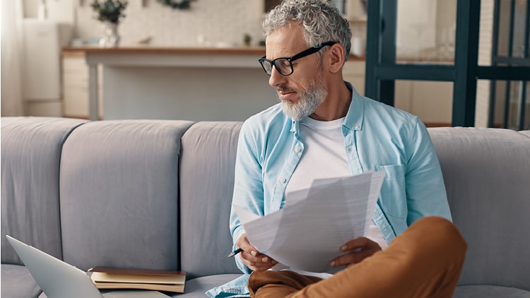 Man sitting on a sofa looking at a laptop and some documents