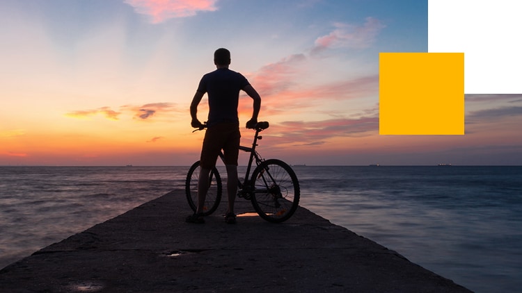 A silhouette of a person cycling beside a pier.