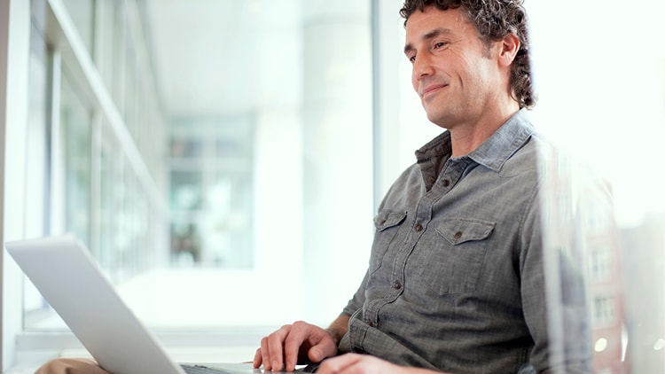 Man sitting at a desk, looking at a laptop