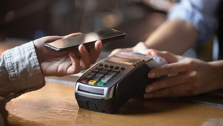 Hand holding a phone over a card reader, paying using contactless payment